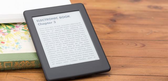 Un lector de libros electrónicos sobre una mesa de madera junto a un libro impreso